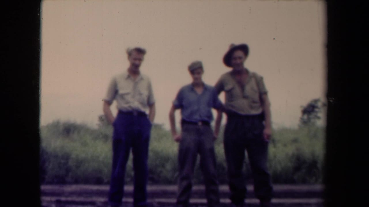 Three men stand on a Papua New Guinea roadside, including one in a wide-brimmed hat and others in cap-like headwear.