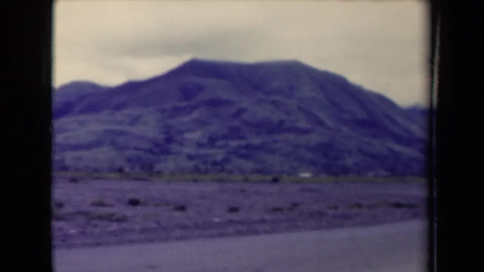 A rugged mountain range in Papua New Guinea appears beyond a road or open ground under an overcast sky.