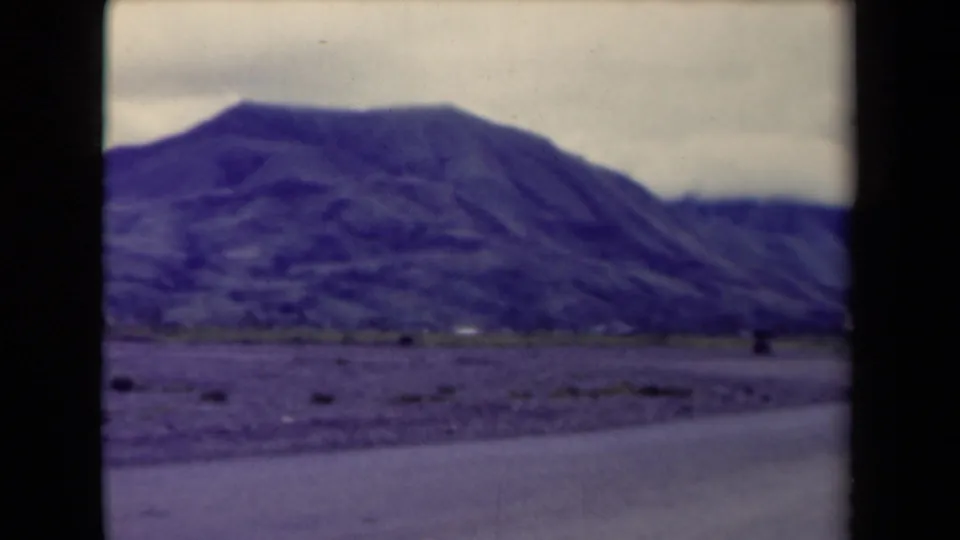 A mountain ridge in Papua New Guinea is filmed from a moving roadside viewpoint, with dark gate edges visible.
