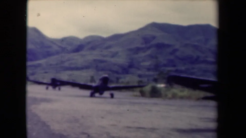 A military aircraft remains on the mountain airfield runway while another plane is partially visible at the right edge of the 8mm frame.