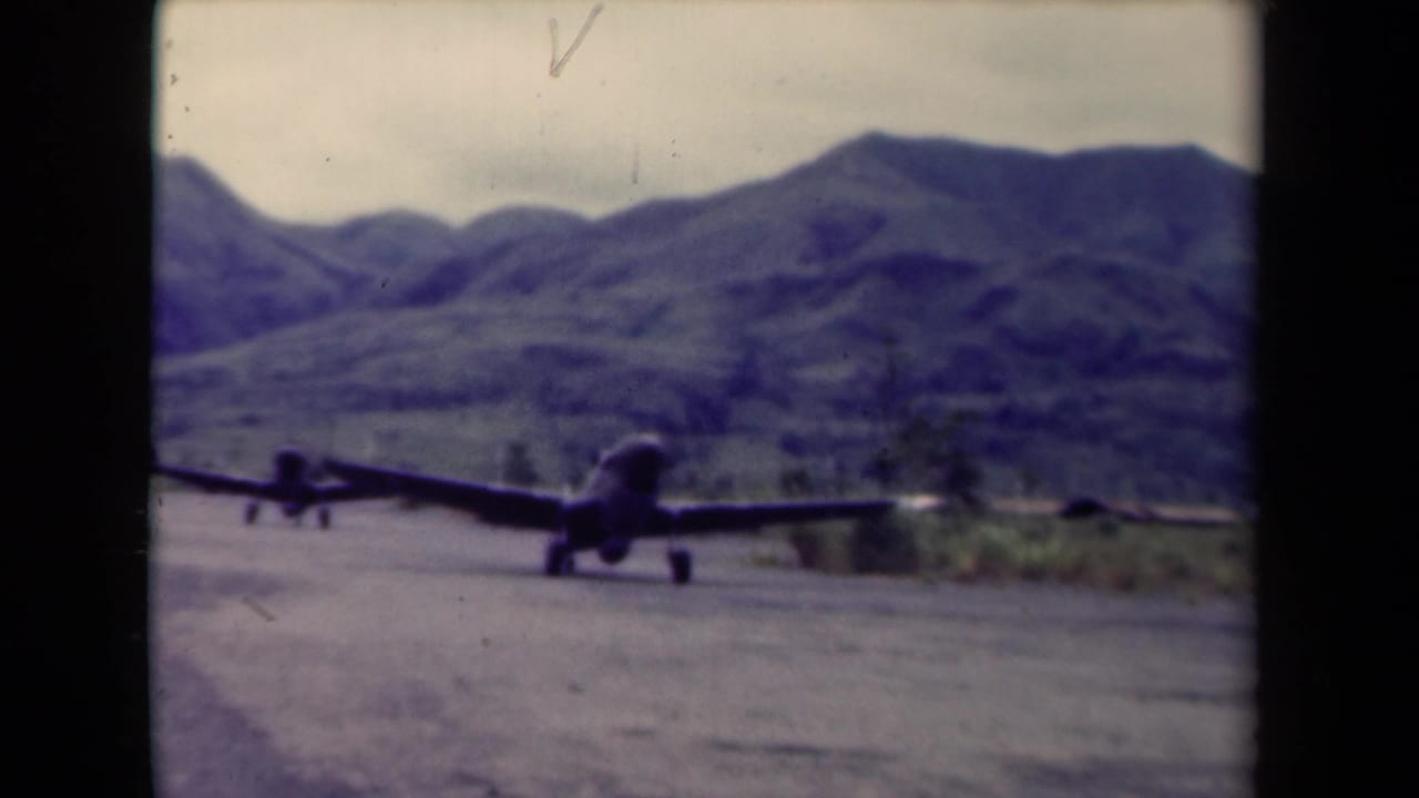 1944 Papua New Guinea 8mm frame showing two military aircraft on a rugged airstrip before rolling hills.