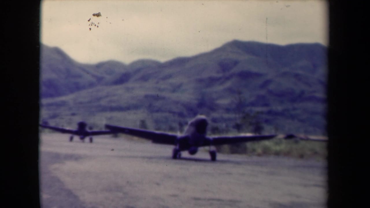 Aircraft on a runway with hills behind and visible 8mm film borders.