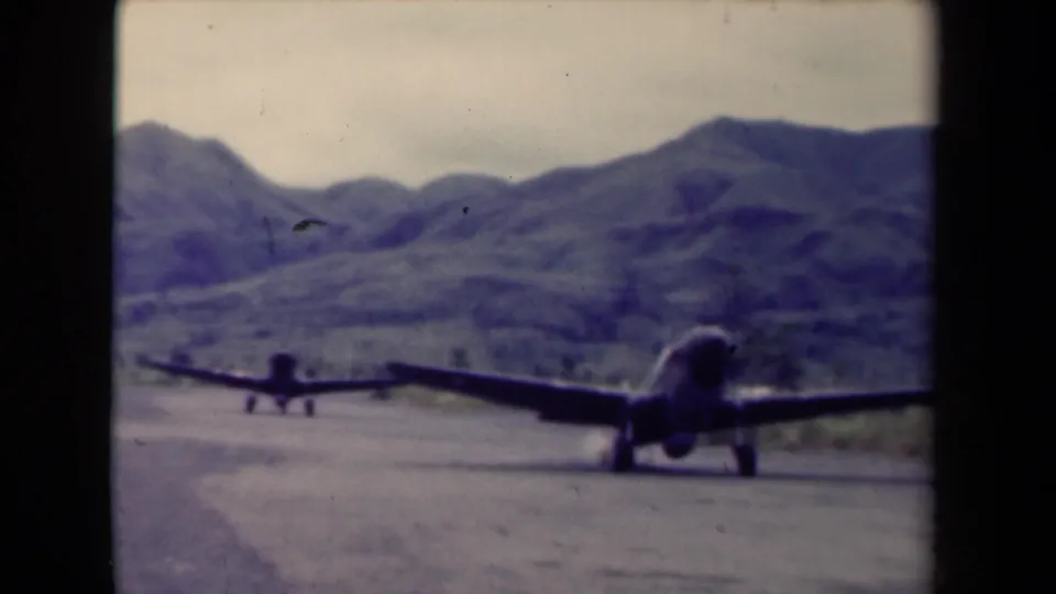 Soft 8mm frame from Papua New Guinea in 1944 showing aircraft on a rugged runway against green hills.