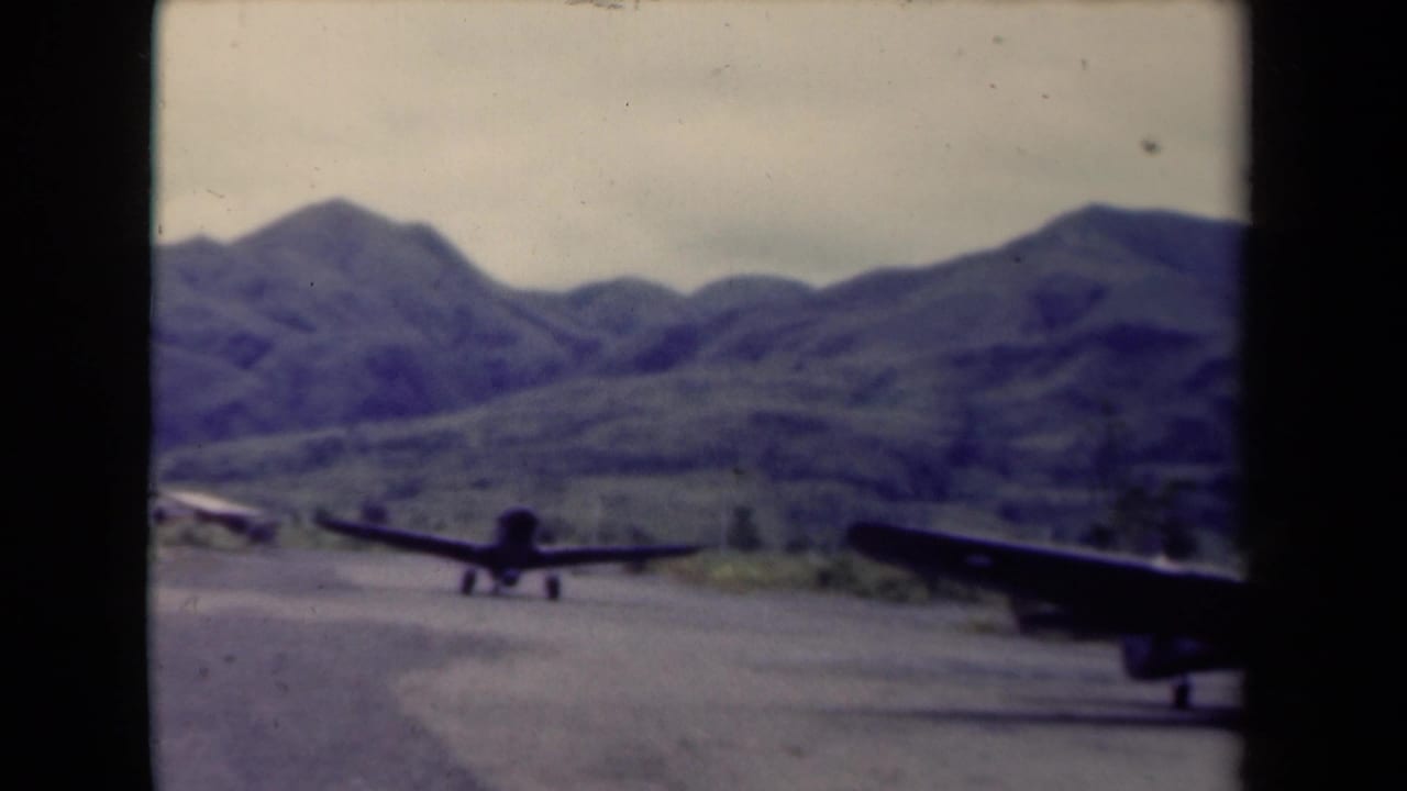 Two aircraft taxi on a rough runway with mountains in the distance.