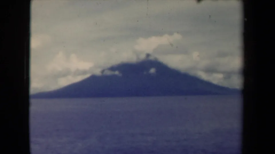 1940s Papua New Guinea 8mm view of a large island across the ocean, its upper slope partly clouded.
