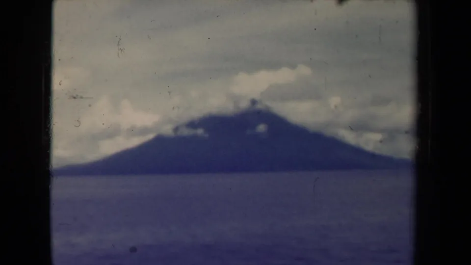 1940s Papua New Guinea coastal view showing a distant island across water with cloud cover near the summit.