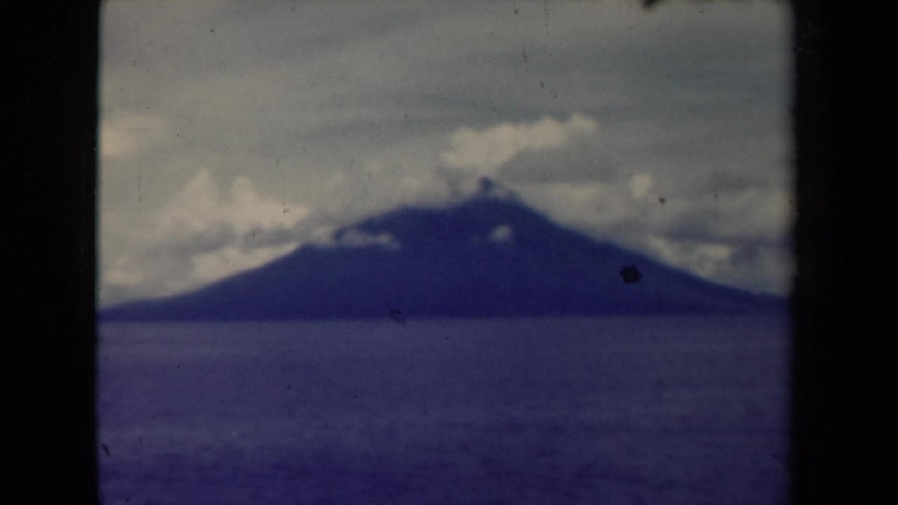 Distant dark mountain across calm sea under clouds, framed by 8mm film borders.