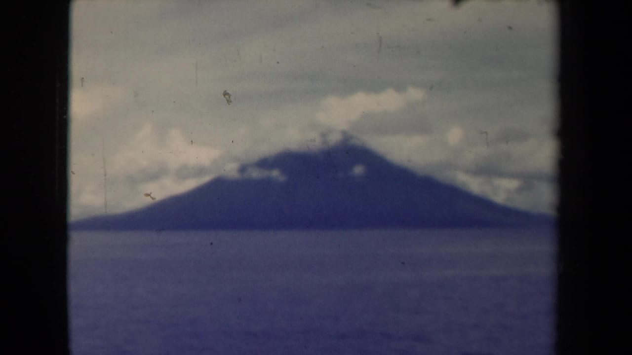Distant mountain across calm water beneath a cloudy sky.