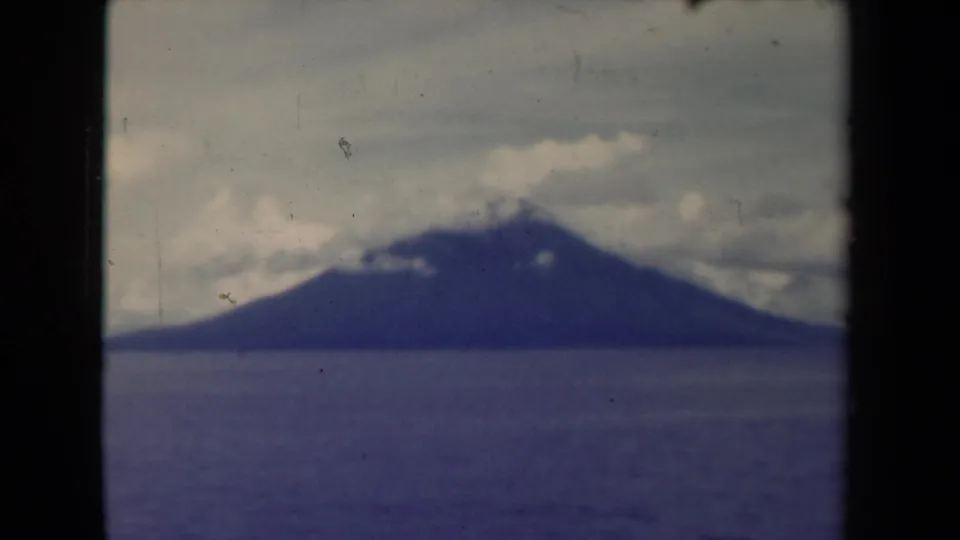 1944 8mm Papua New Guinea footage showing a distant mountain across calm water with clouds near the summit.