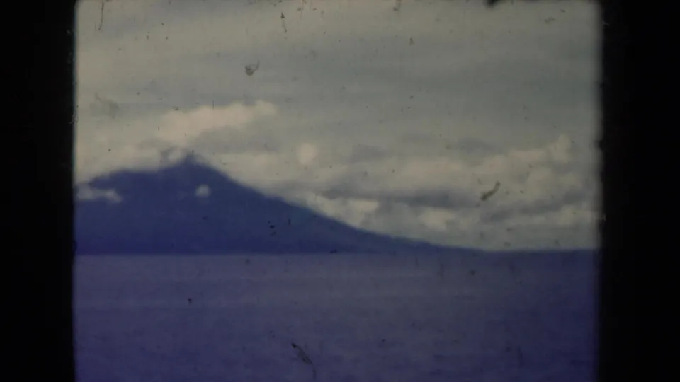 End frame of 1944 Papua New Guinea 8mm footage with a distant mountain, calm water, low clouds, and aged film texture.
