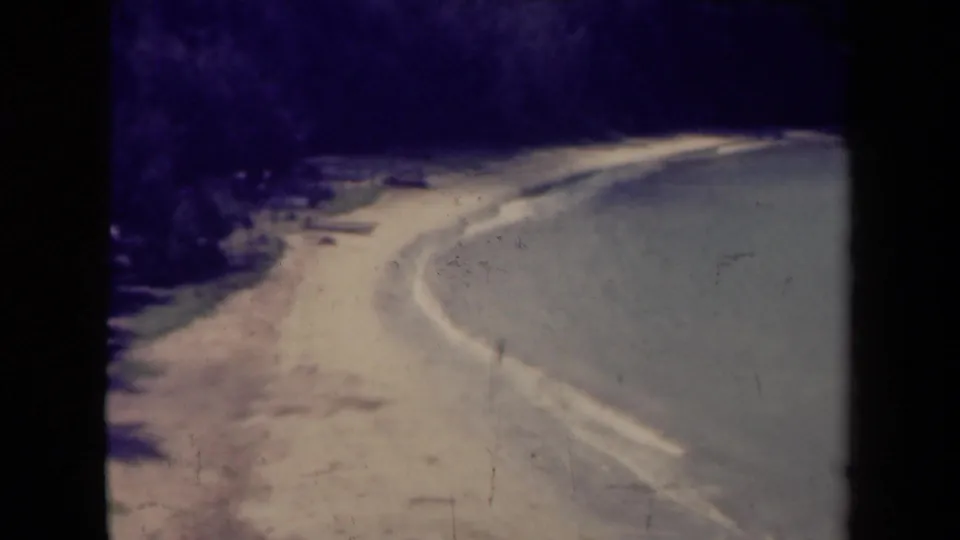 1940s Kauai home-movie frame showing a soft, shadowed road curve with a pale shoulder and dark vegetation at left.