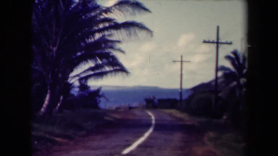 1944 Kauai home-movie frame of a road bending through tropical vegetation toward distant water or mountains.