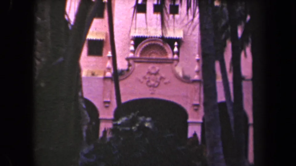 Ornate pink facade and shaded arched doorway viewed through trees in archival Hawaii footage.