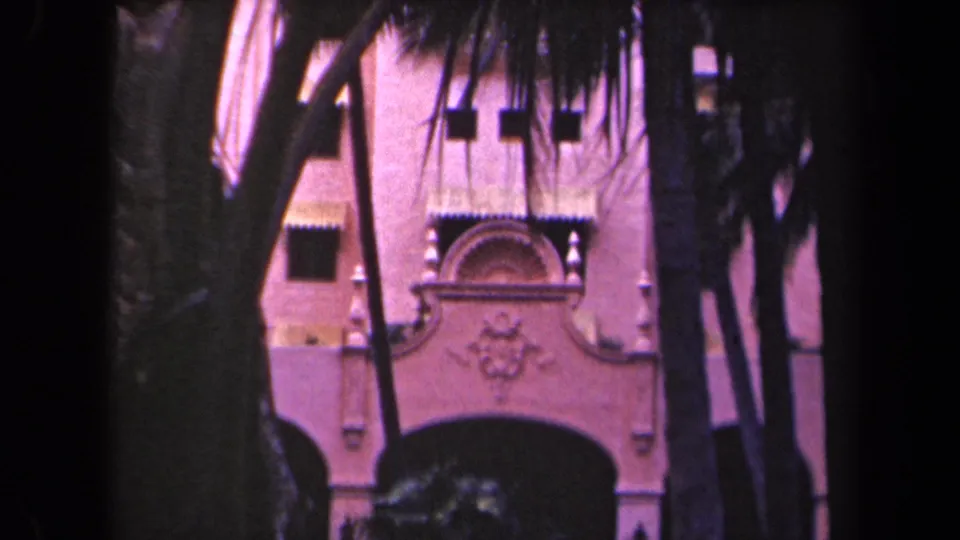 Pink stucco building with decorative arch and palm-framed entrance in 1940s Hawaii home-movie footage.