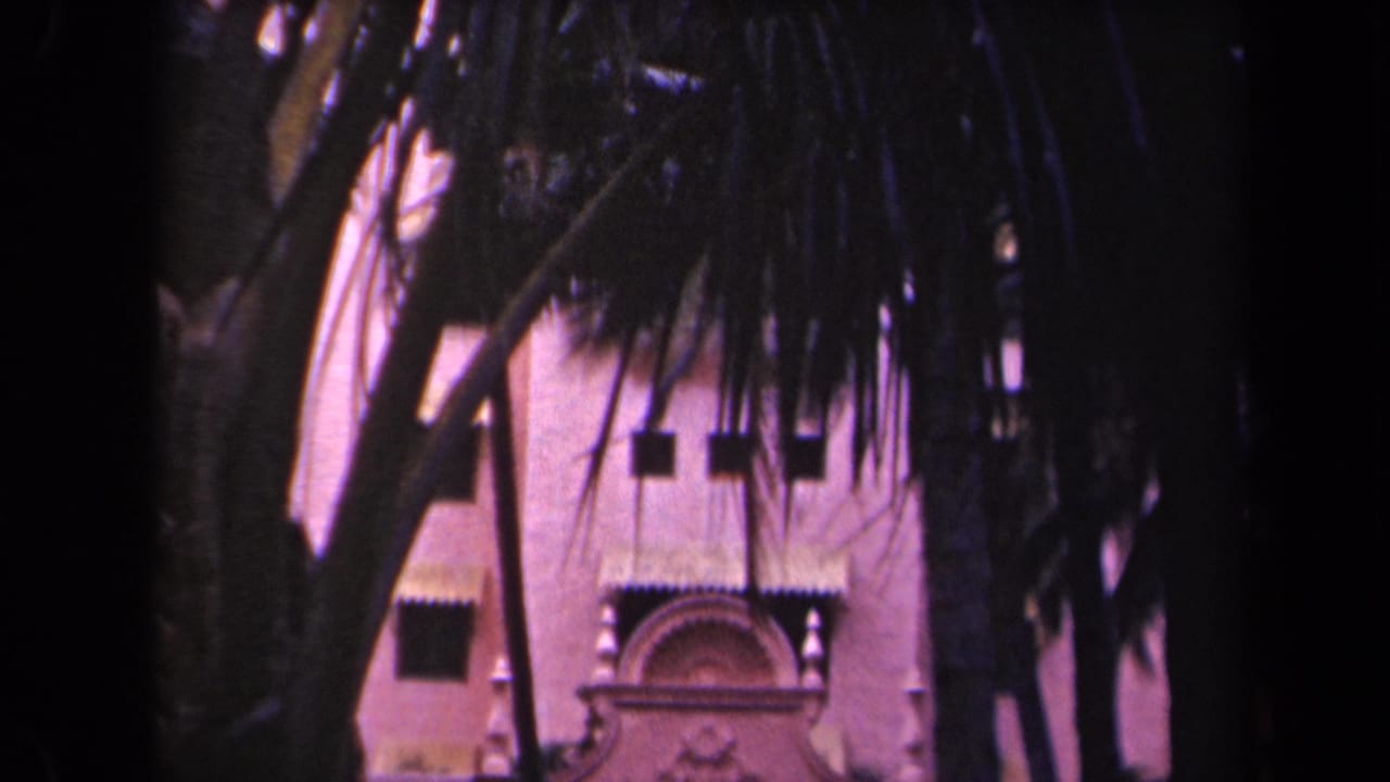 Palm-shaded view of a Kauai resort facade with decorative stucco work and arched walkways, from 1944 8mm footage.
