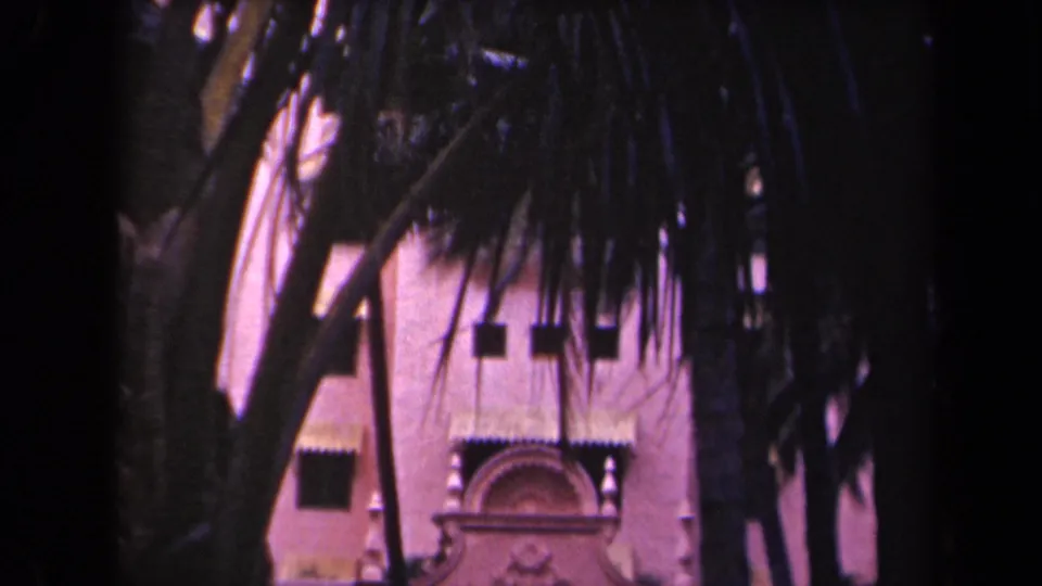Palm-shaded view of a Kauai resort facade with decorative stucco work and arched walkways, from 1944 8mm footage.