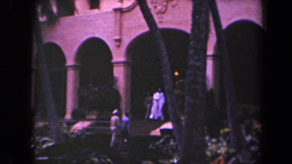 Kauai resort courtyard in 1944 with small figures in light clothing beneath arched stucco walkways and palms.