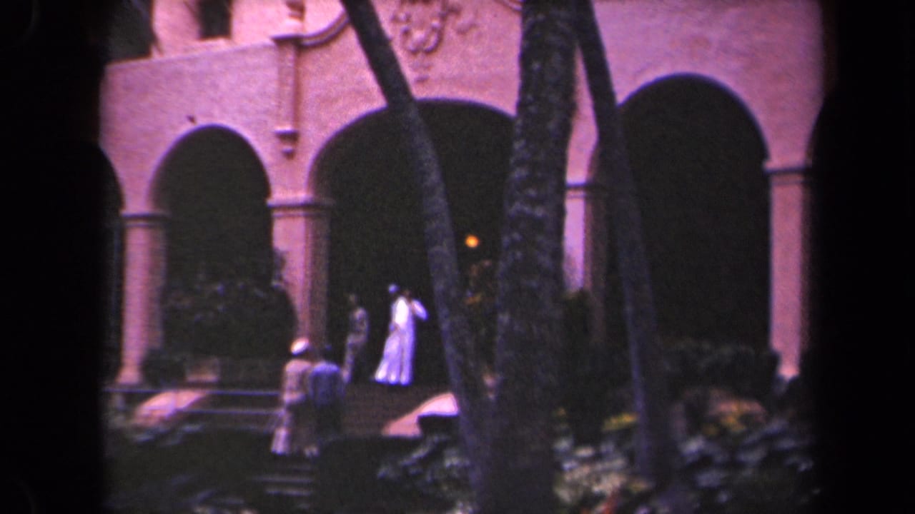 1944 Kauai home-movie frame showing visitors near steps and dark arches of a pink-toned historic-looking building.