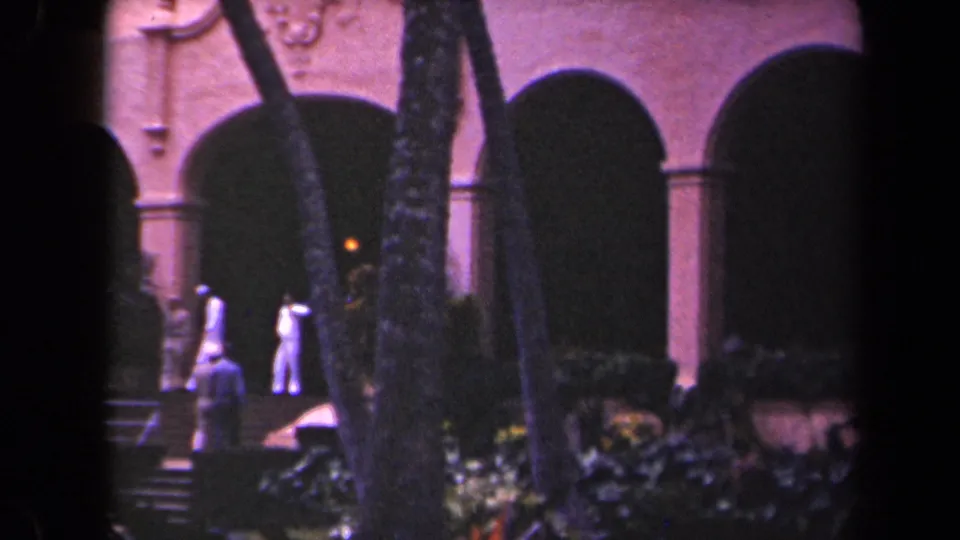 Visitors in light clothing pass through a palm-framed courtyard toward arched building entrances in Kauai, Hawaii.