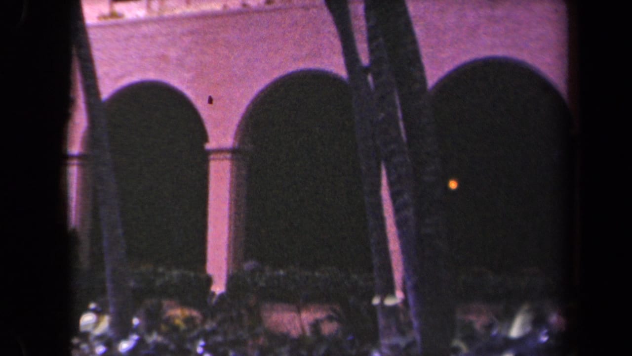 1944 Kauai 8mm frame showing arched architecture behind dark tropical foliage, with soft focus and saturated color.