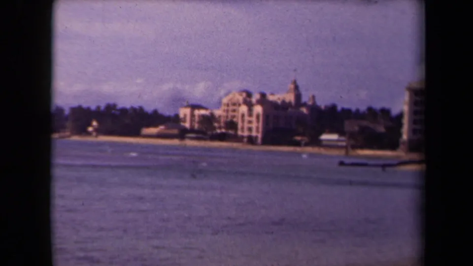 1940s Hawaii home-movie frame of Waikiki Beach hotels and shoreline viewed from across calm blue water.