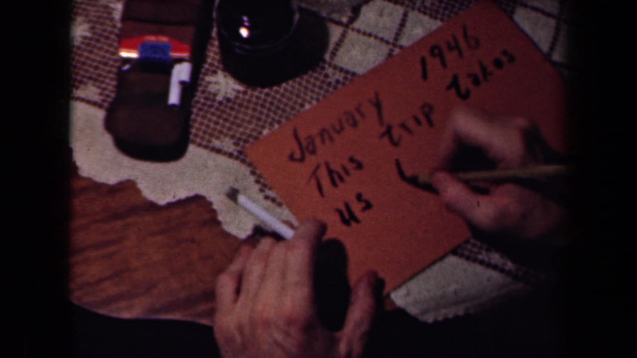Hands write on a brown card reading January 1946 on a patterned tabletop.