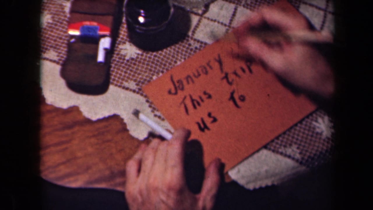 Adult hands steady a brown card with partially written text, including January and trip wording, on a domestic tabletop.