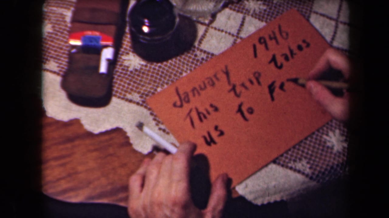 Hands continue adding text to a brown card that reads as a January 1946 trip to France note, filmed close-up on 8mm.