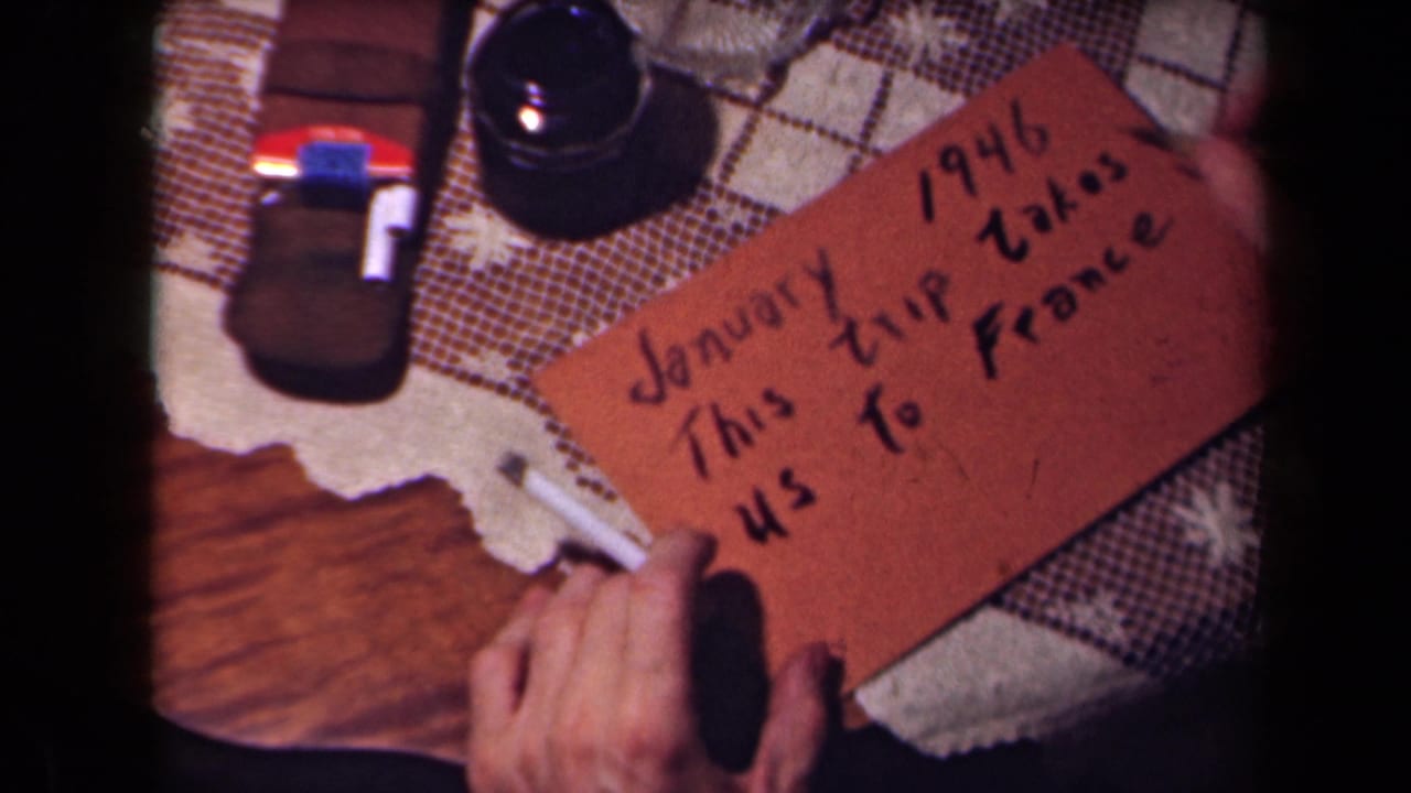 The brown card now clearly states a January 1946 trip to France, held by hands in a close 8mm tabletop shot.
