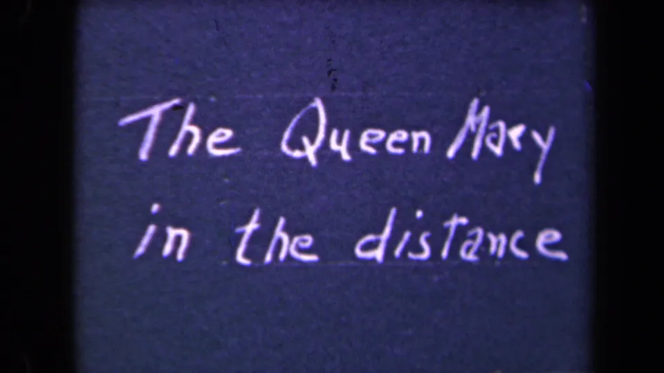 1945 8mm title card with white handwritten text reading The Queen Mary in the distance against a dark blue field.