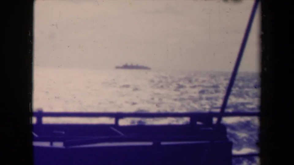 1945 France 8mm frame showing a distant ship at sea beyond a dark deck rail and diagonal rigging line.