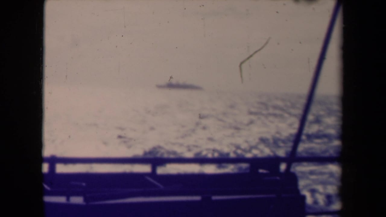 1945 France 8mm frame with a distant vessel, choppy sea, dark boat rail, and visible film wear.