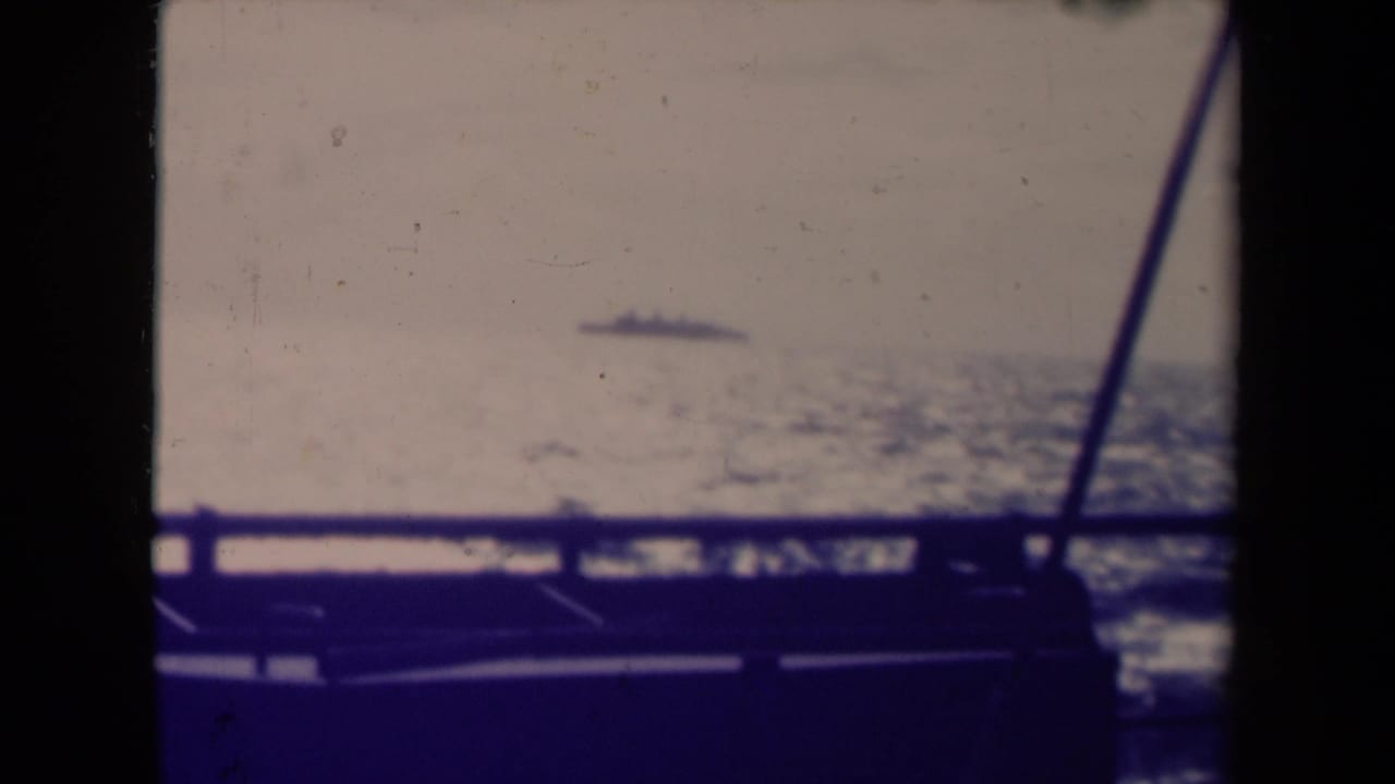 1945 France 8mm frame showing a small ship on the horizon, foreground rail, soft sea texture, and faded color.