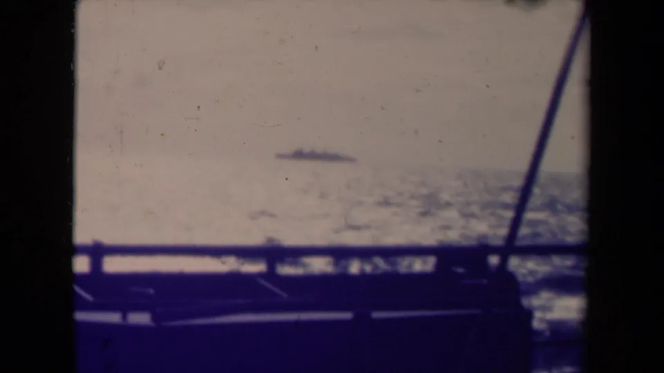 1945 France 8mm frame showing a small ship on the horizon, foreground rail, soft sea texture, and faded color.