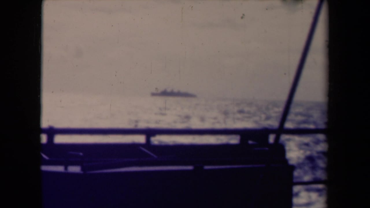 Distant ship on a hazy sea, seen past dark boat railing and supports.