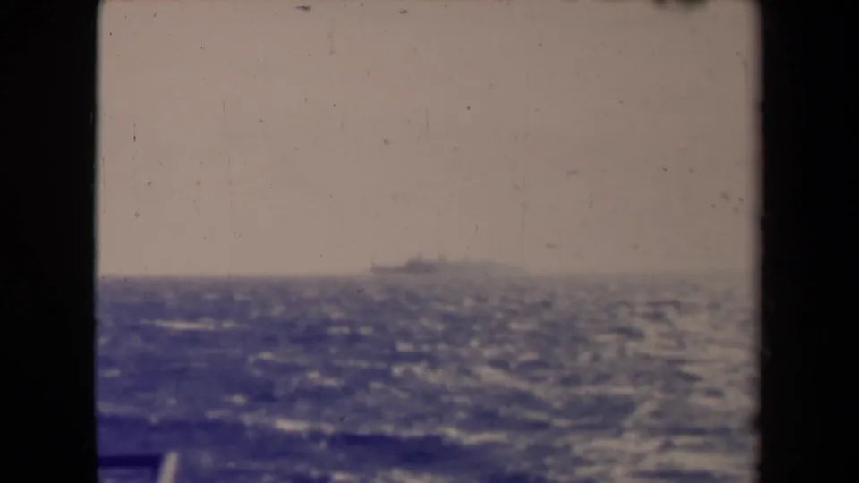 A hazy 1945 France sea view from a moving vessel, with a faint ship near the horizon and dark framing from the boat.