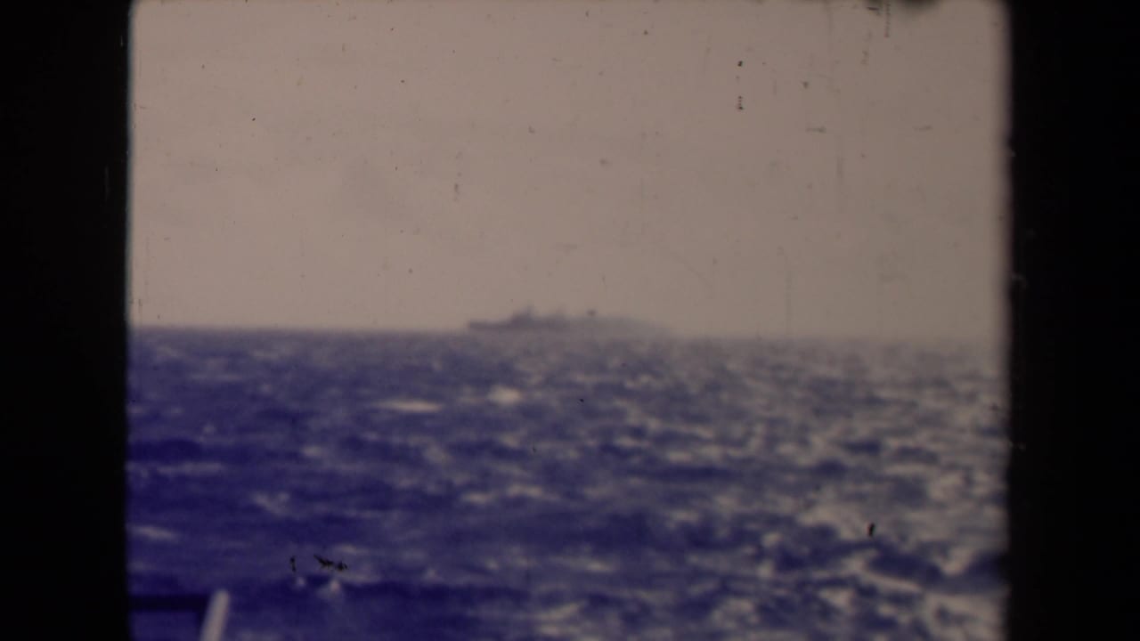 Distant ship on the horizon beyond rough blue water and a dark window frame.