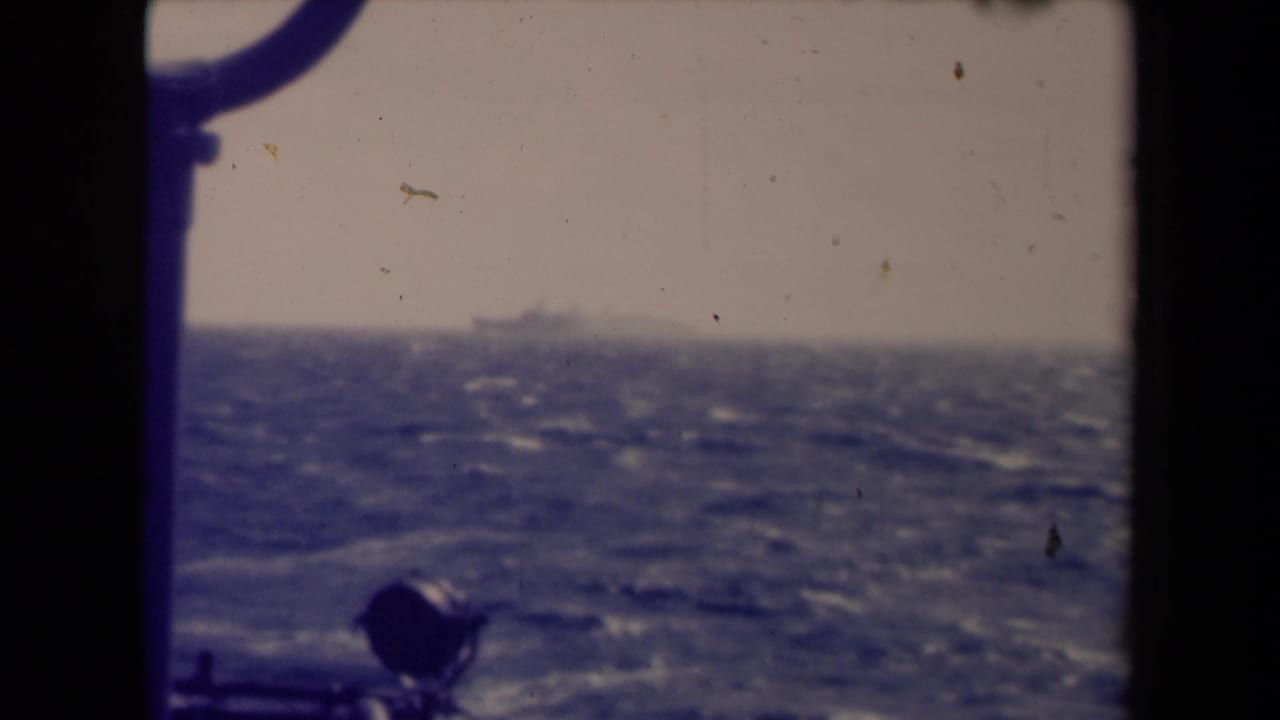 France 1945 8mm frame showing a distant ship over choppy water, with window hardware or rigging in the foreground.