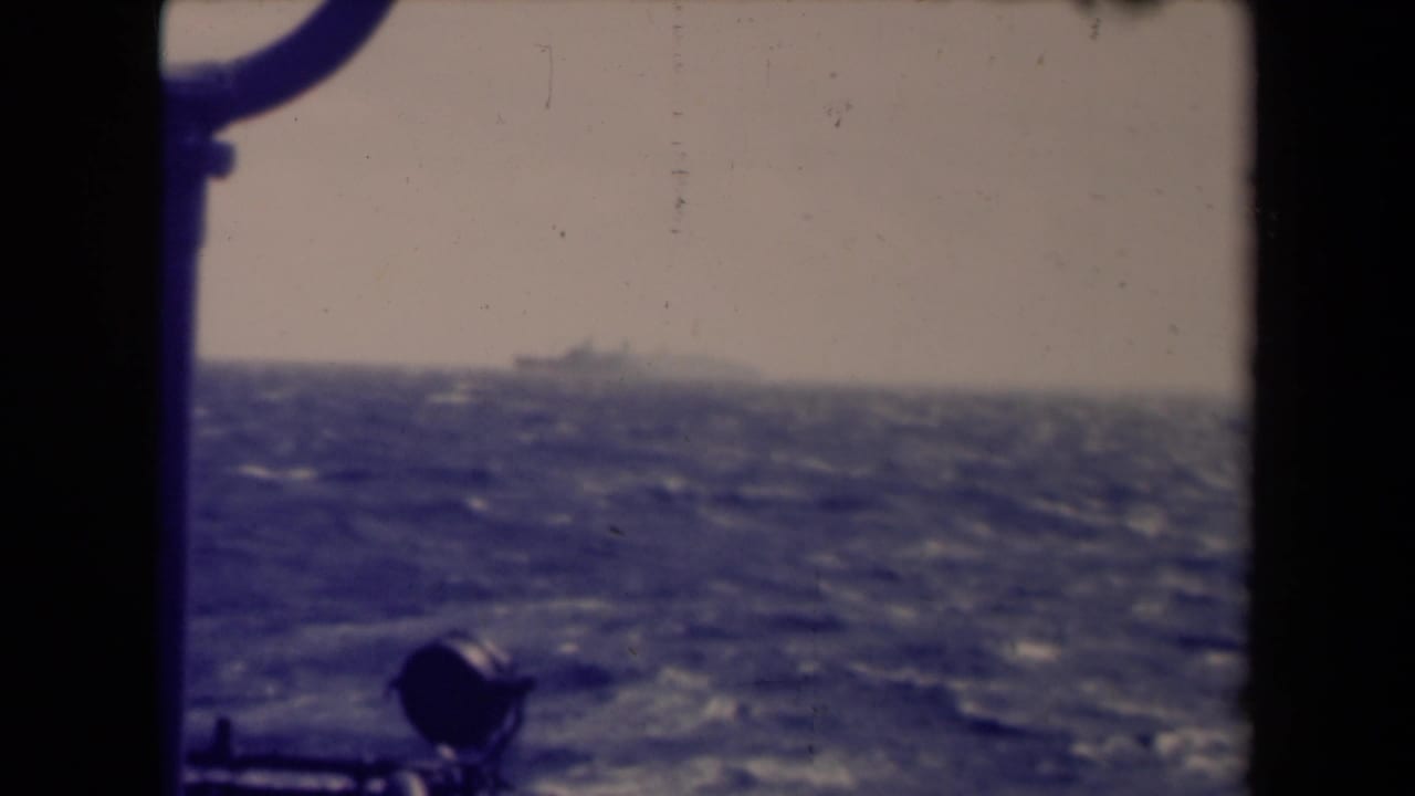 Distant ship on a choppy sea seen past dark shipboard railing.