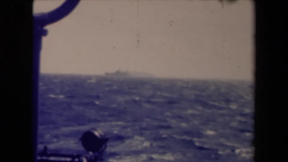 1945 8mm view from a ship near France, with a distant vessel on the horizon beyond choppy water and dark rail hardware.