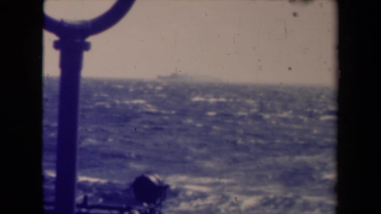 Final 1945 shipboard view of a distant vessel on the horizon, with choppy sea, hazy sky, and 8mm film marks.