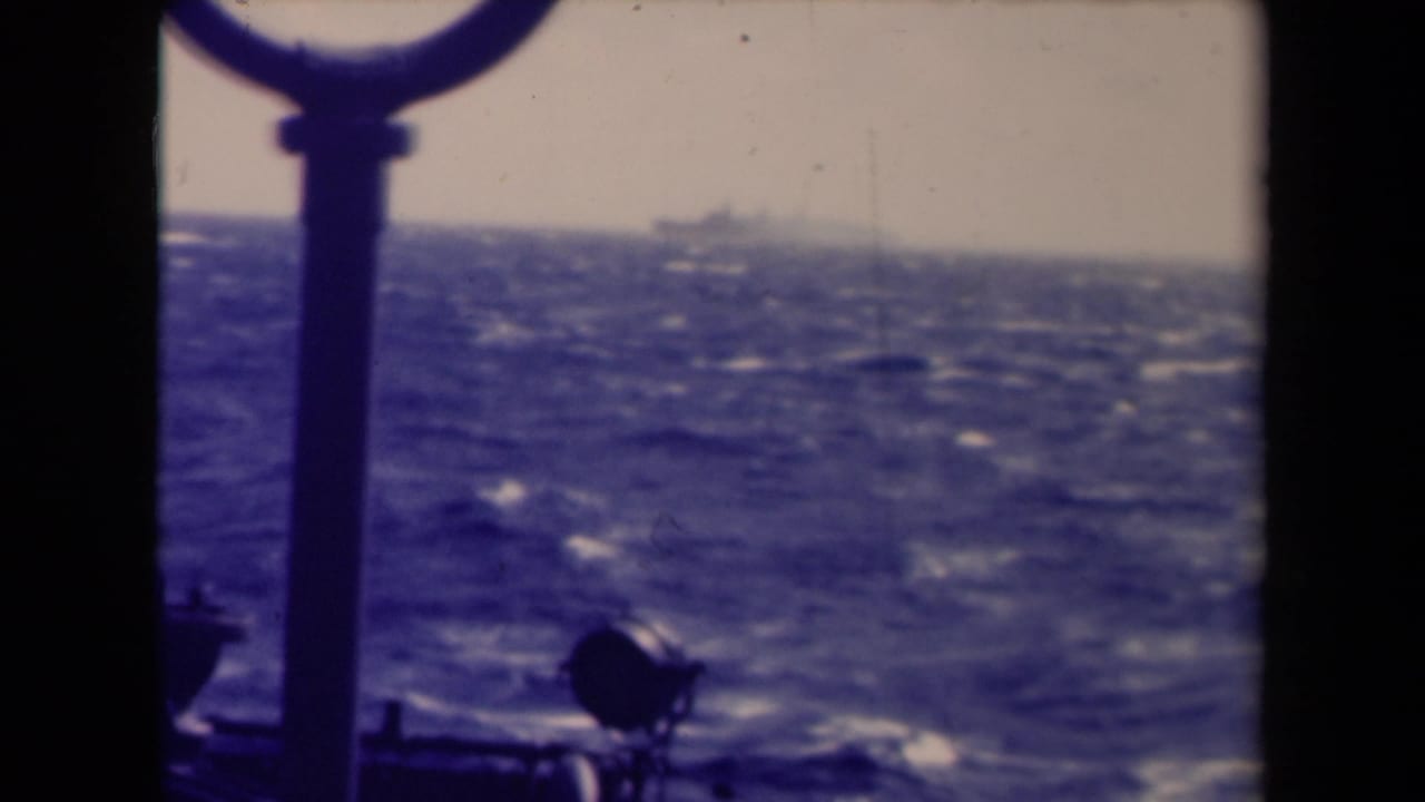Choppy open water framed by dark ship fittings, with a small vessel shape near the horizon.