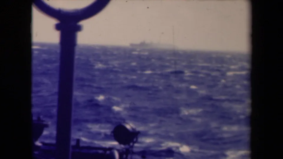 Shipboard 8mm view near France metadata location, with rough blue water, whitecaps, and silhouetted rail hardware in the foreground.