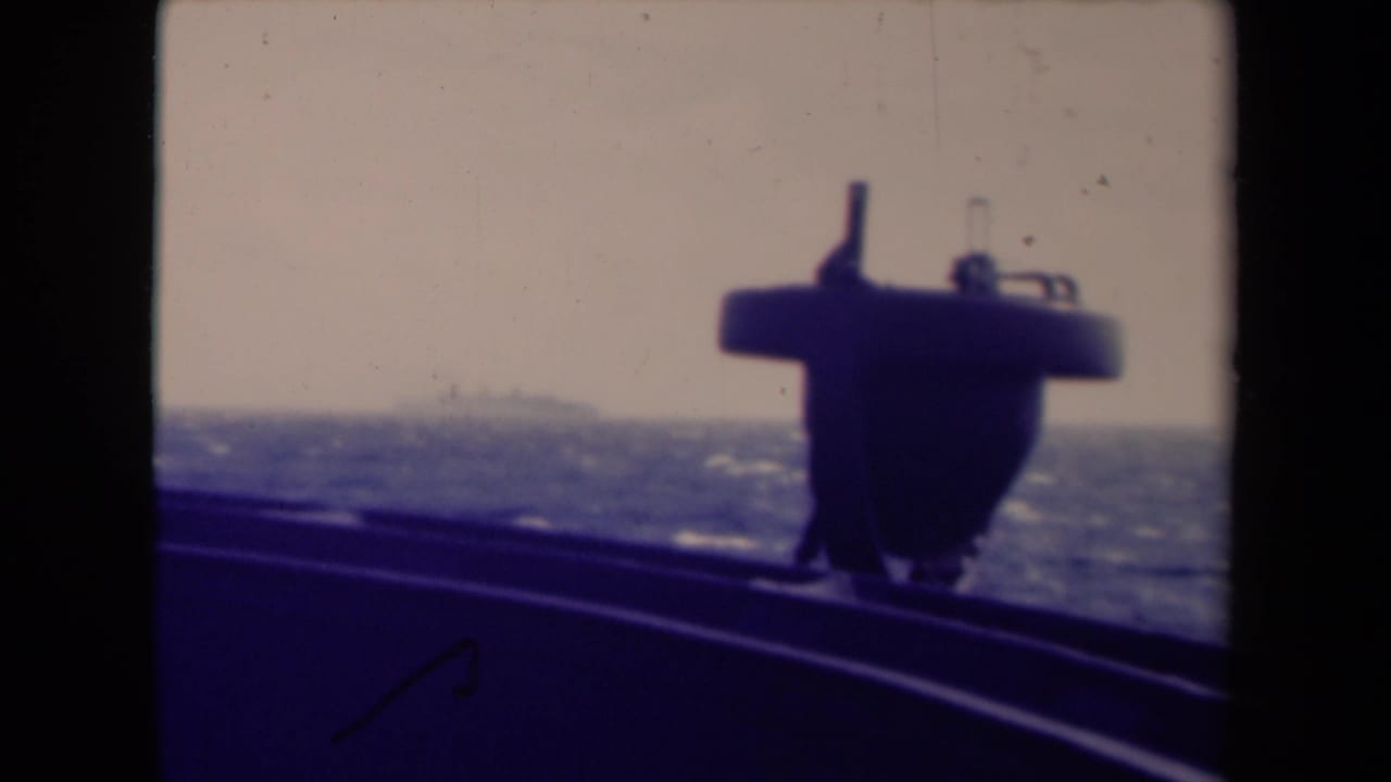 Shipboard view over choppy sea with a dark deck structure and distant horizon.