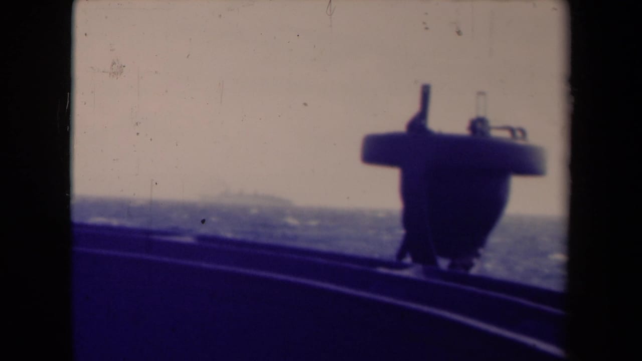 Final shipboard frame with a dark structure in front, choppy sea below, and a faint distant vessel or shoreline shape near the horizon.