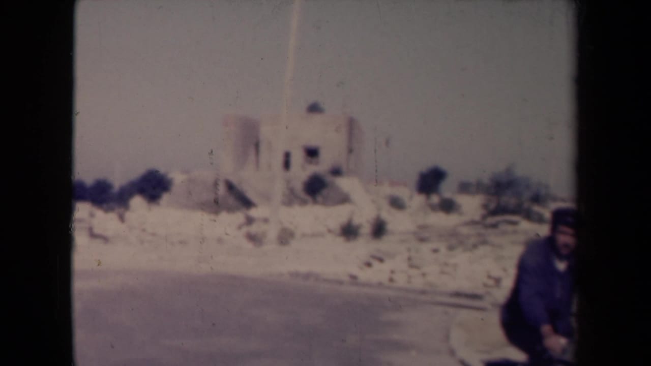 Cyclist partly at the right edge with a pale building and sparse ground behind him.