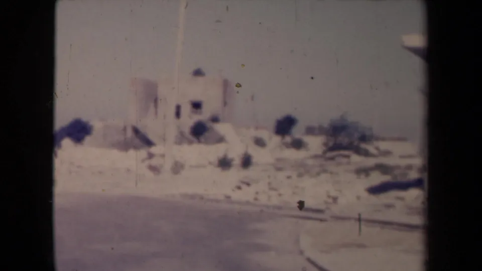 A dusty road curves past a pale church-like building in a dry French landscape recorded on soft color home-movie film.