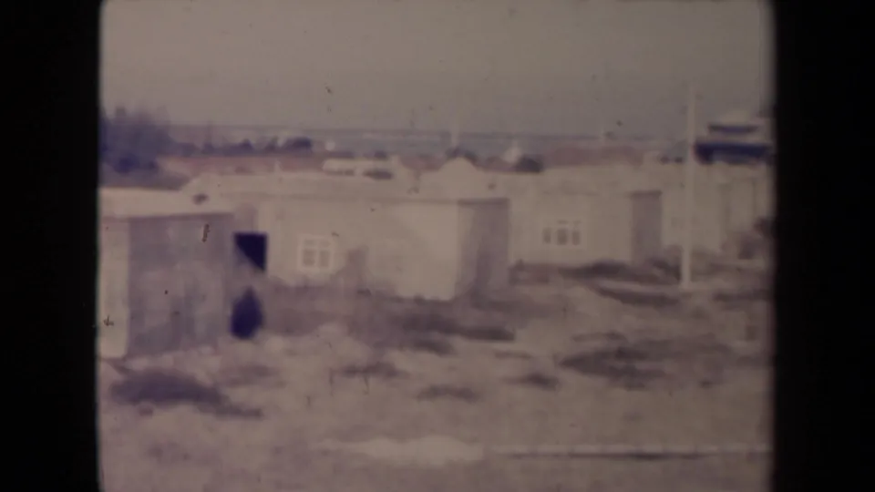 1945 France home-movie frame showing low deteriorated housing, dark window openings and bare terrain in soft focus.