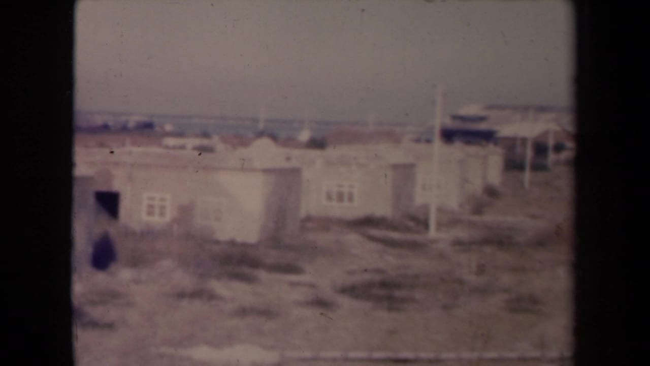 Low worn buildings with dark openings and sparse ground in front.