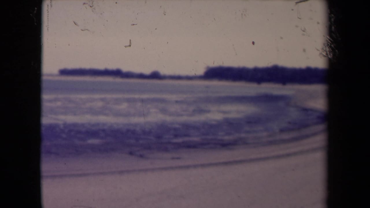 1945 France frame of a calm shoreline with water, distant land and visible 8mm frame edges.